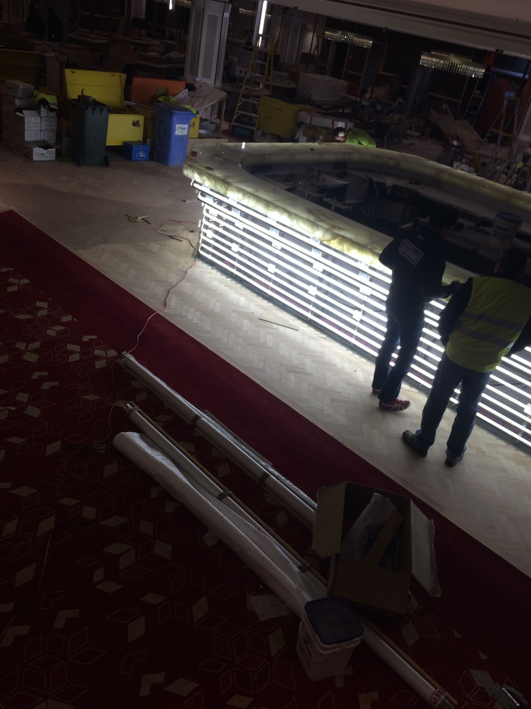 Two people examining bright stacked metal bars in a dim warehouse-like space
