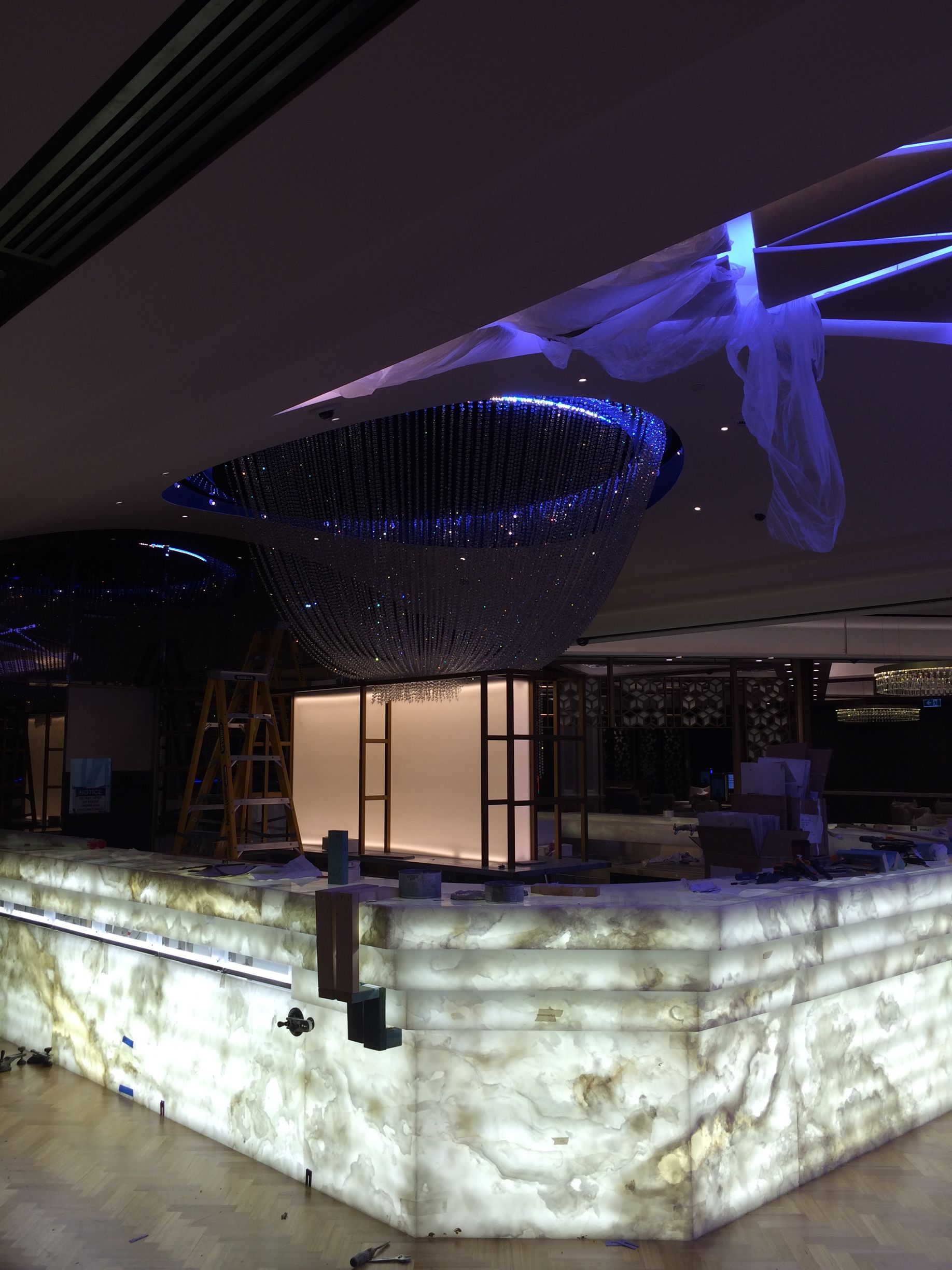 Modern indoor art installation with glowing white pedestal and blue-lit abstract sculpture suspended overhead