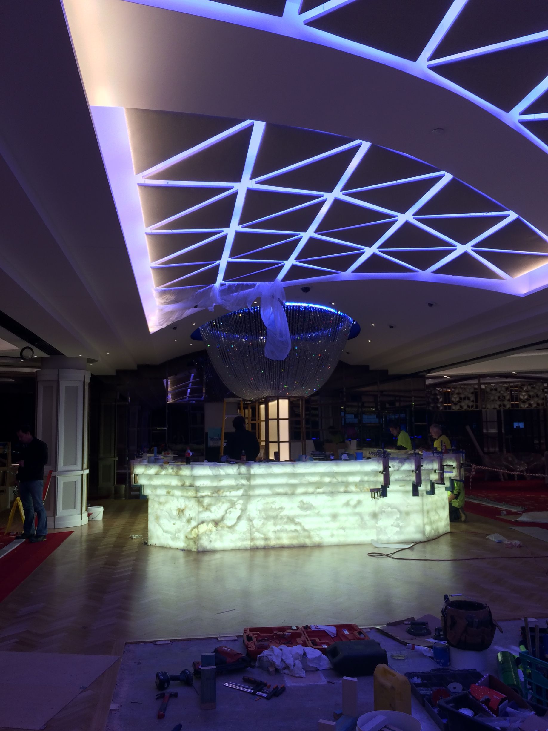 Neon-lit bar with glowing counter, geometric ceiling lights, and a disco ball in a dark club interior