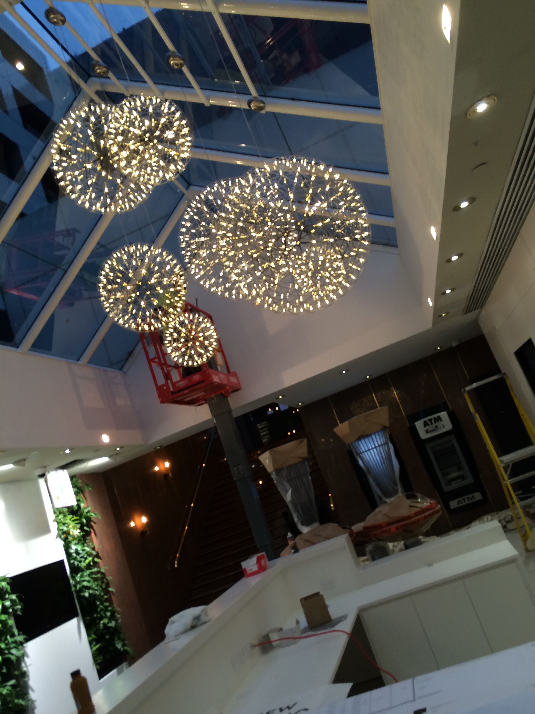 Modern lounge with glowing chandelier lights and white seating under a glass ceiling