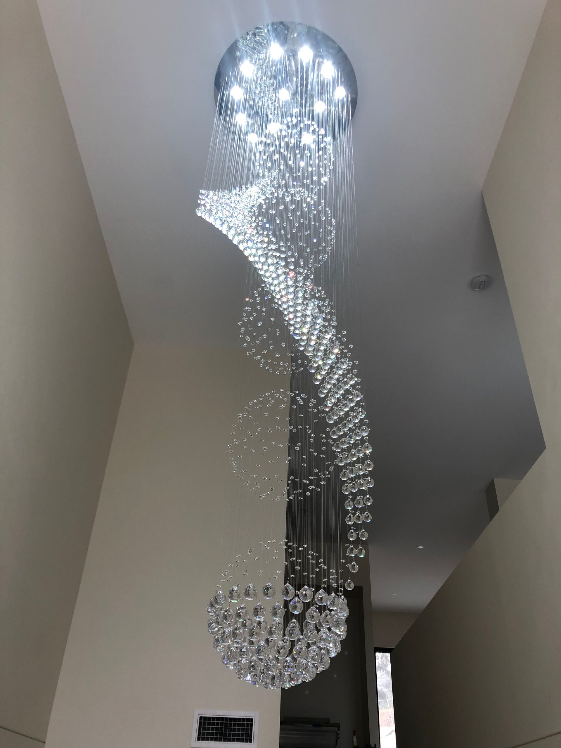 Tall spiral crystal chandelier hanging from a ceiling in a modern interior hallway