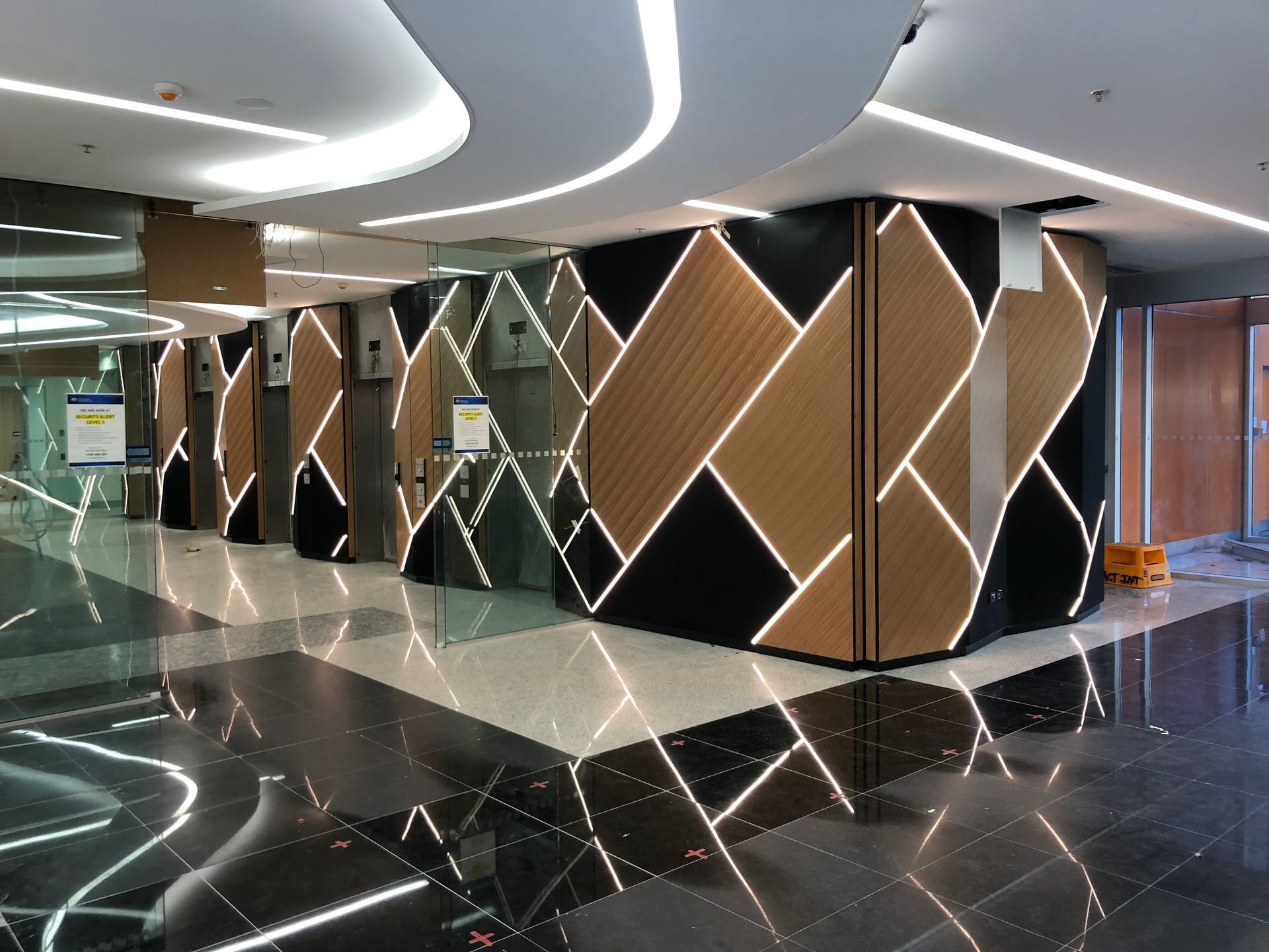 Modern lobby with glossy black floor, curved ceiling lights, and faceted geometric wall panels in gold and dark tones
