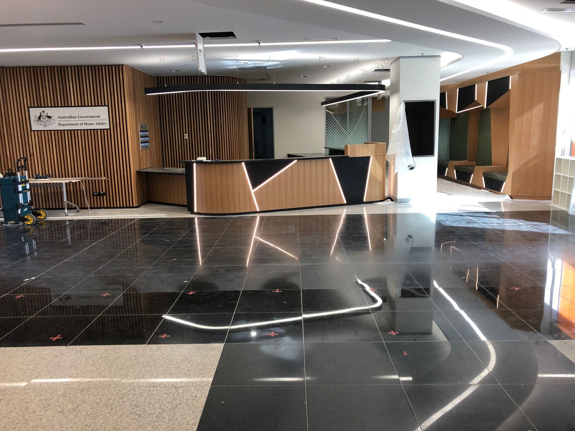 Modern lobby with glossy black floor, wood-paneled reception desk, and white ceiling lighting