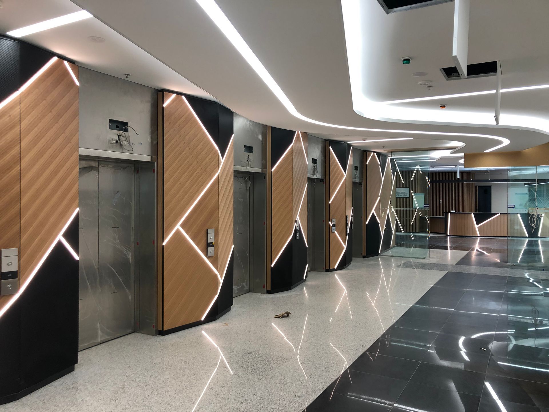 Modern elevator lobby with wood-paneled shafts, glossy black floor, and curved ceiling lights