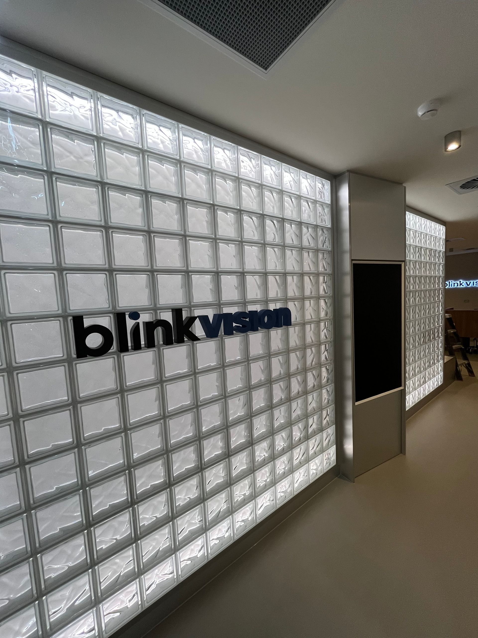 Blink branding on a glass-block wall in a hallway with beige floor and ceiling lights