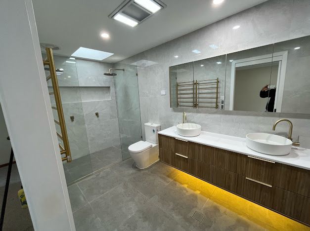 Modern bathroom with double vanity, large mirror, glass shower, and gray tile flooring