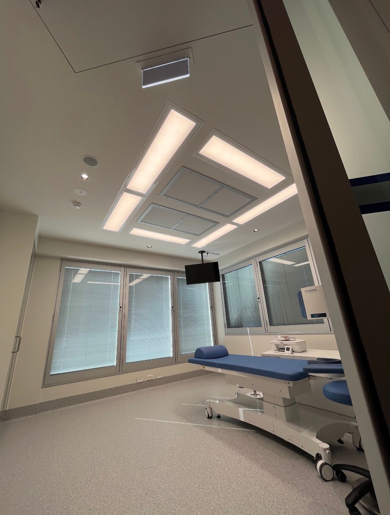 Modern hospital operating room with surgical table, overhead lights, and large window blinds