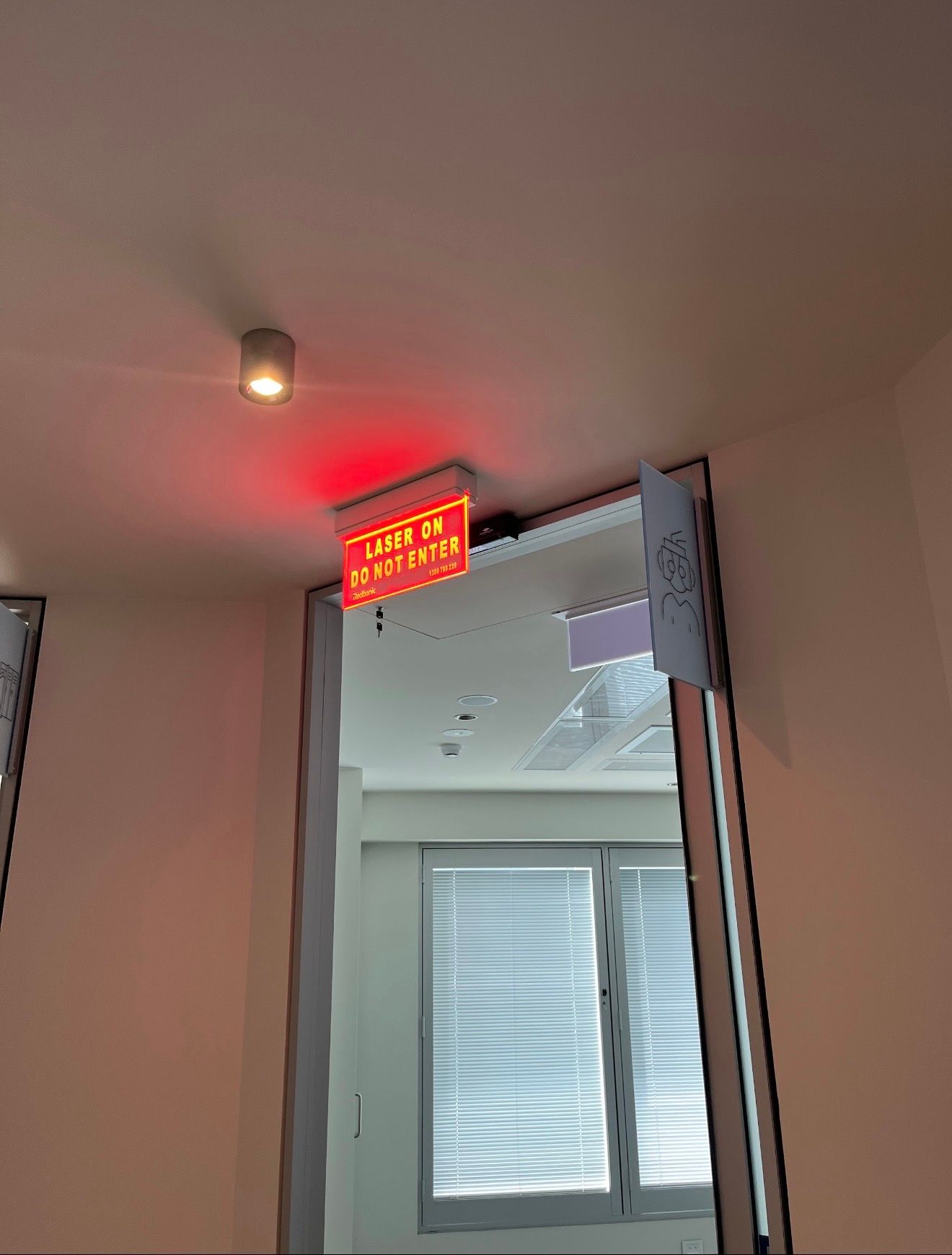 Red exit sign above an open doorway in a white indoor hallway.