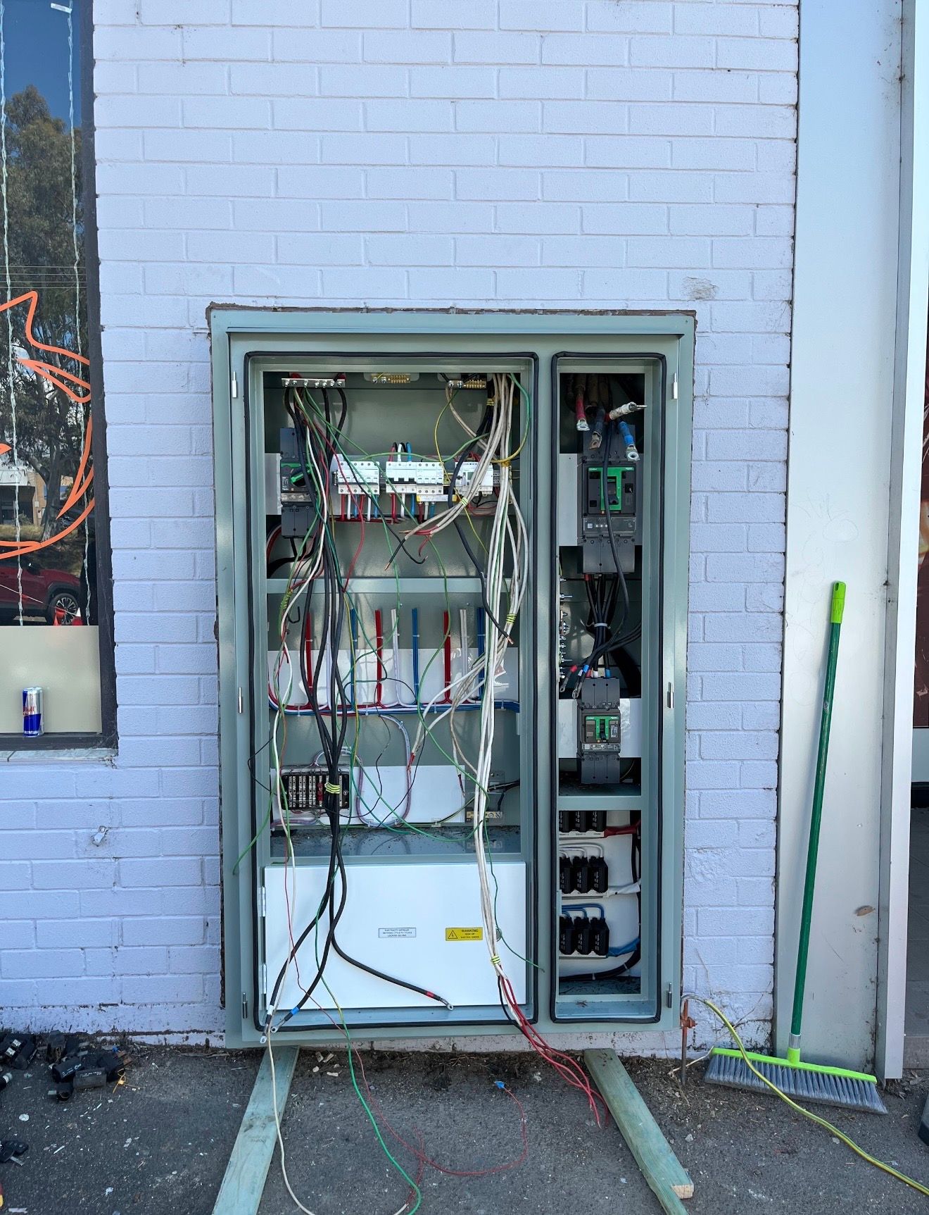 Open electrical panel cabinet on a light blue brick wall with exposed wiring and equipment in a utility area