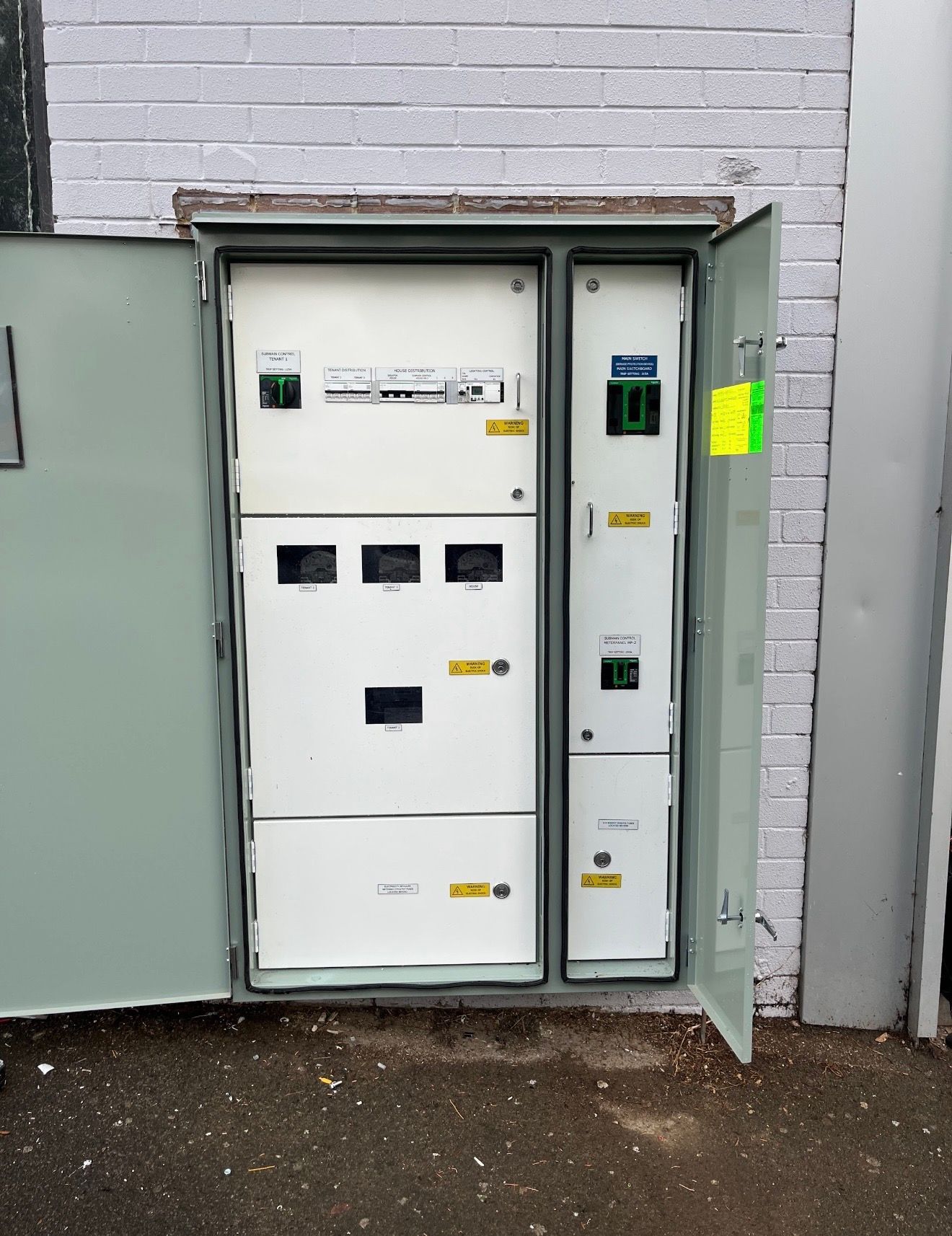 Open electrical utility cabinets on a concrete wall, with one door ajar and control panels visible.