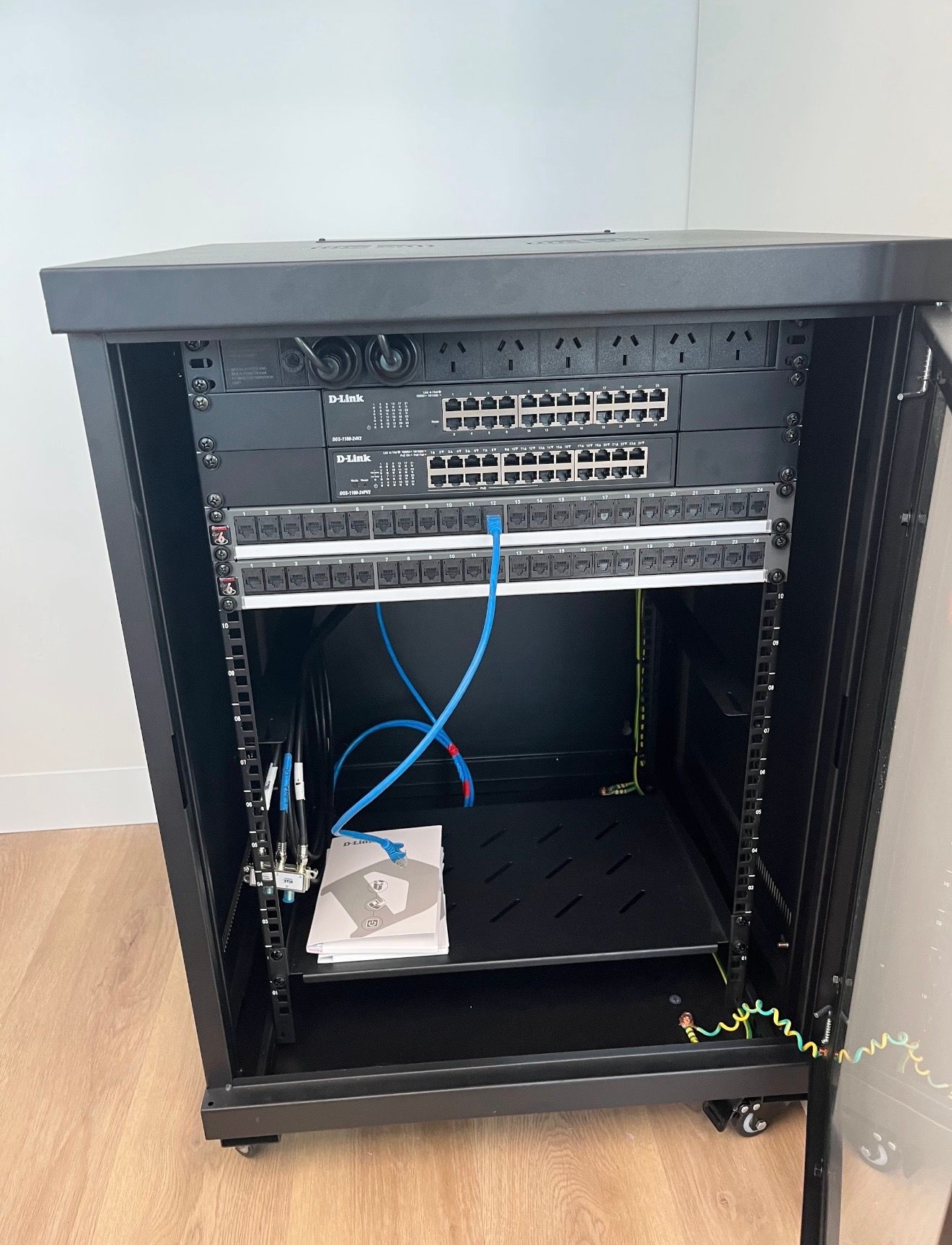Open network rack with switches and blue cables on a wooden floor