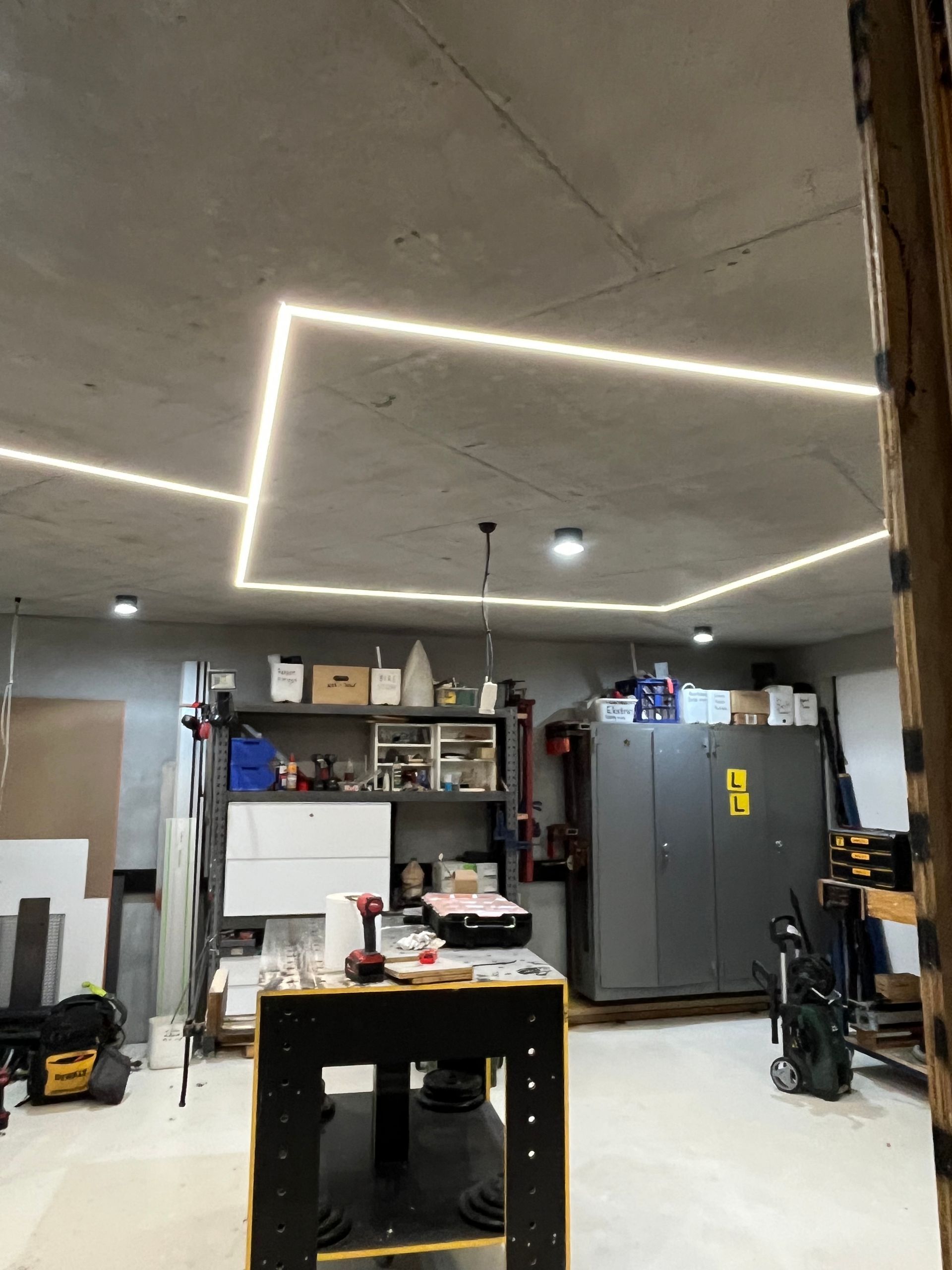 Garage workshop with LED ceiling lights, shelves, tools, and a large gray cabinet.