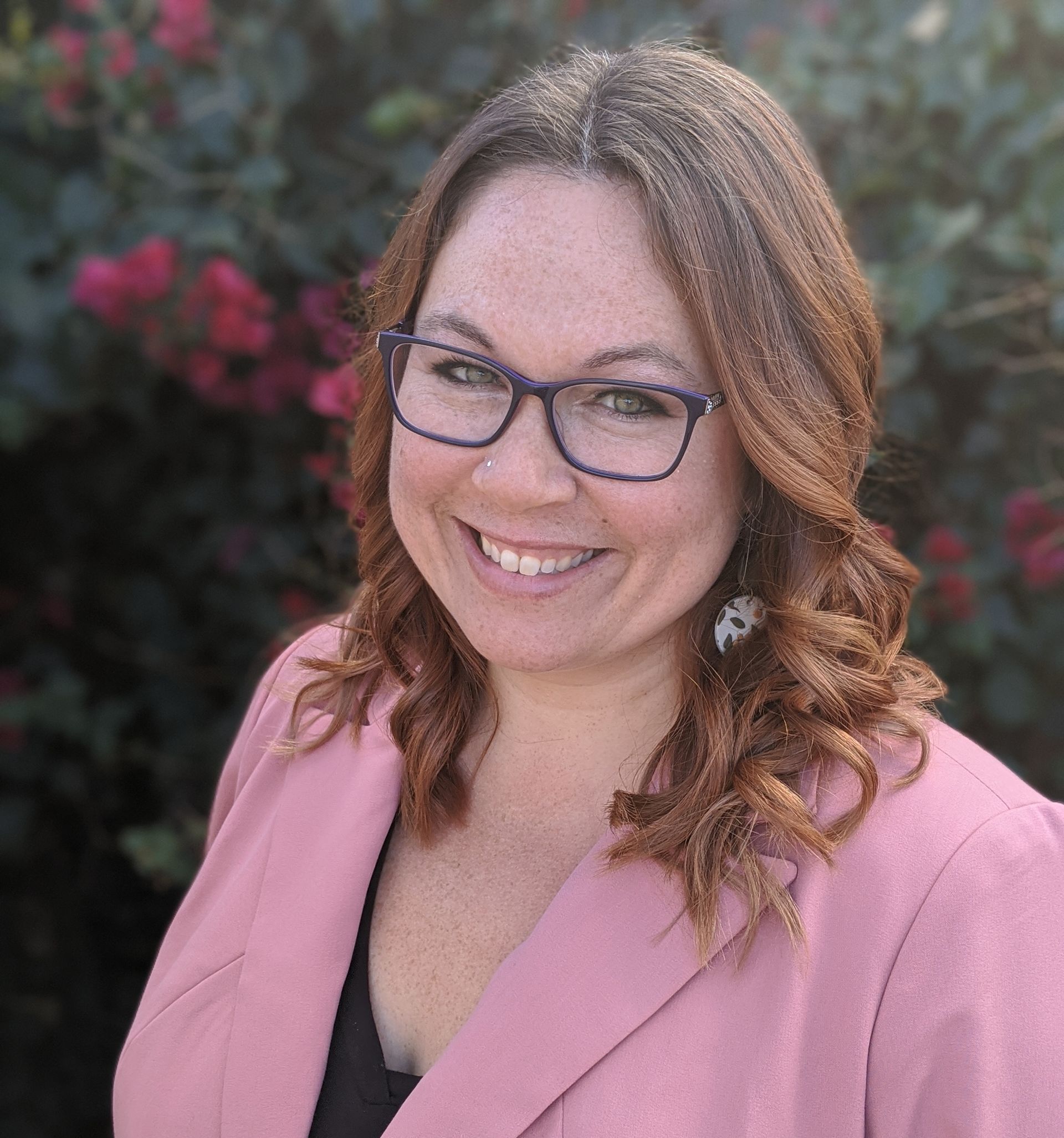 Roya Dedeaux LMFT wearing glasses and a pink jacket is smiling for the camera.