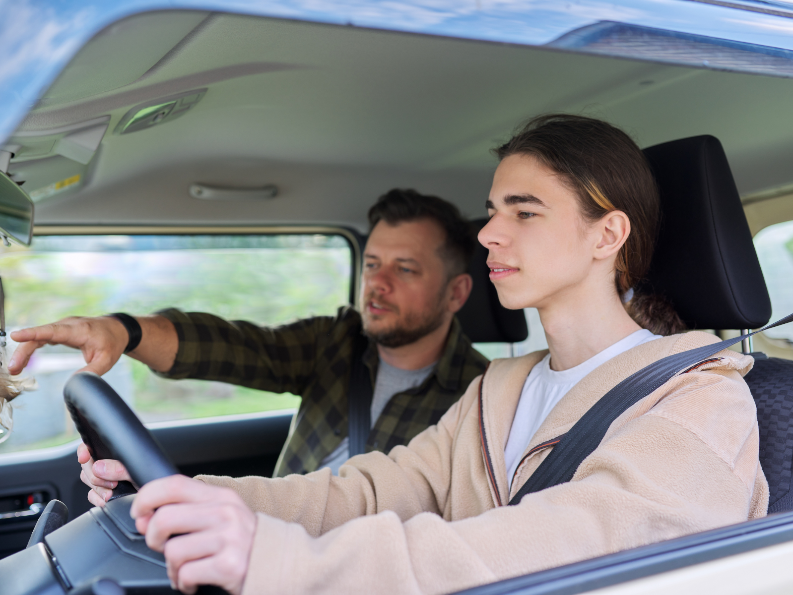 A man is teaching a young girl how to drive a car.