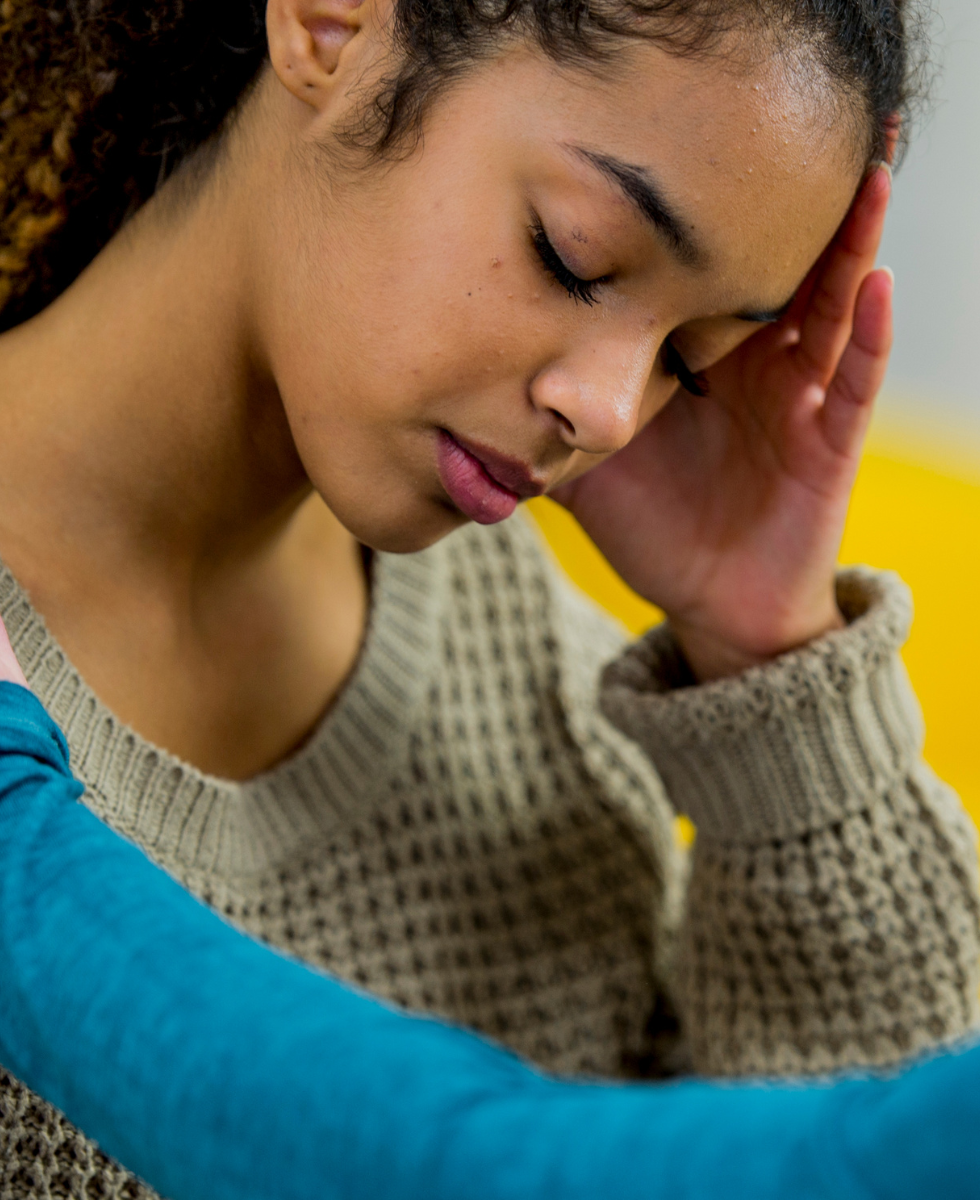 A woman in a sweater is covering her face with her hand.