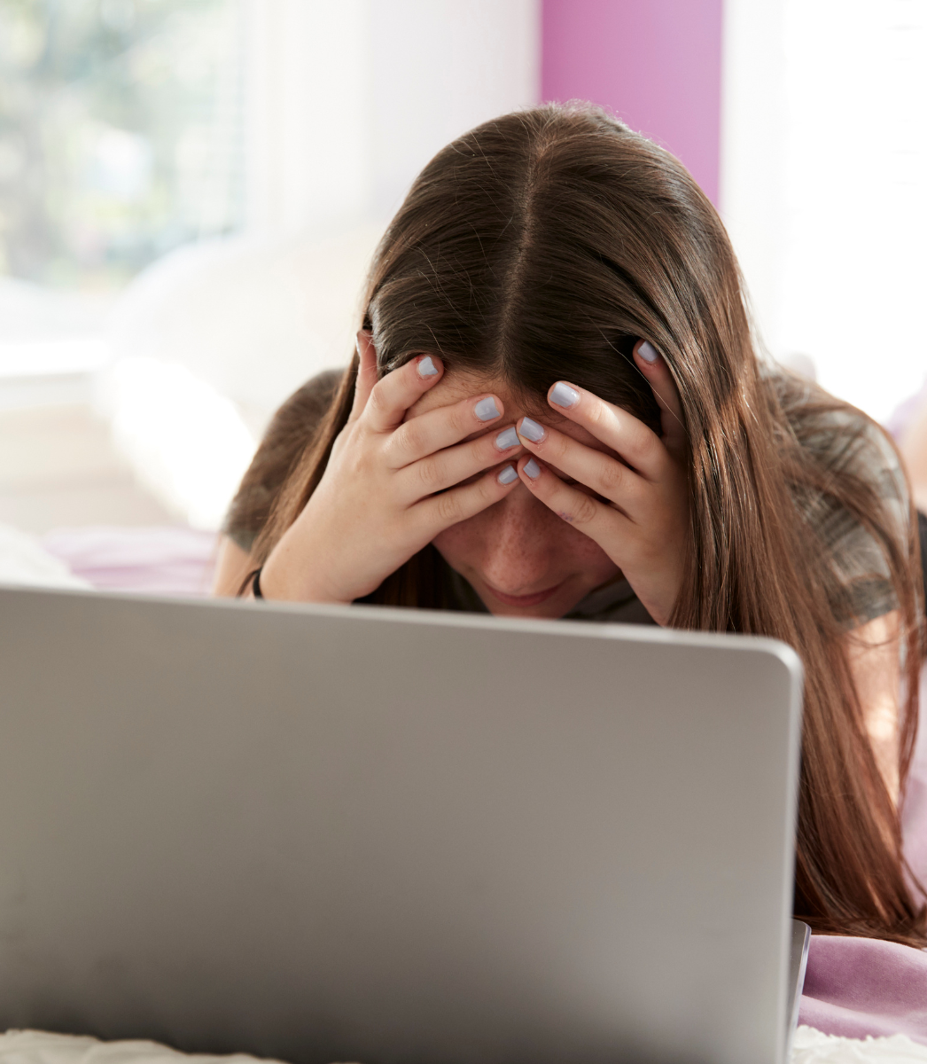 A woman is covering her face while using a laptop computer