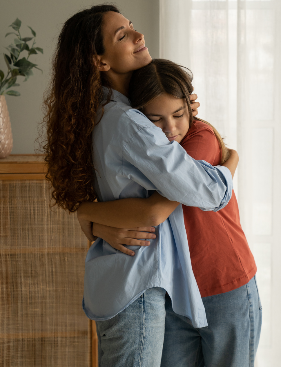 A woman is hugging a young girl in a living room.
