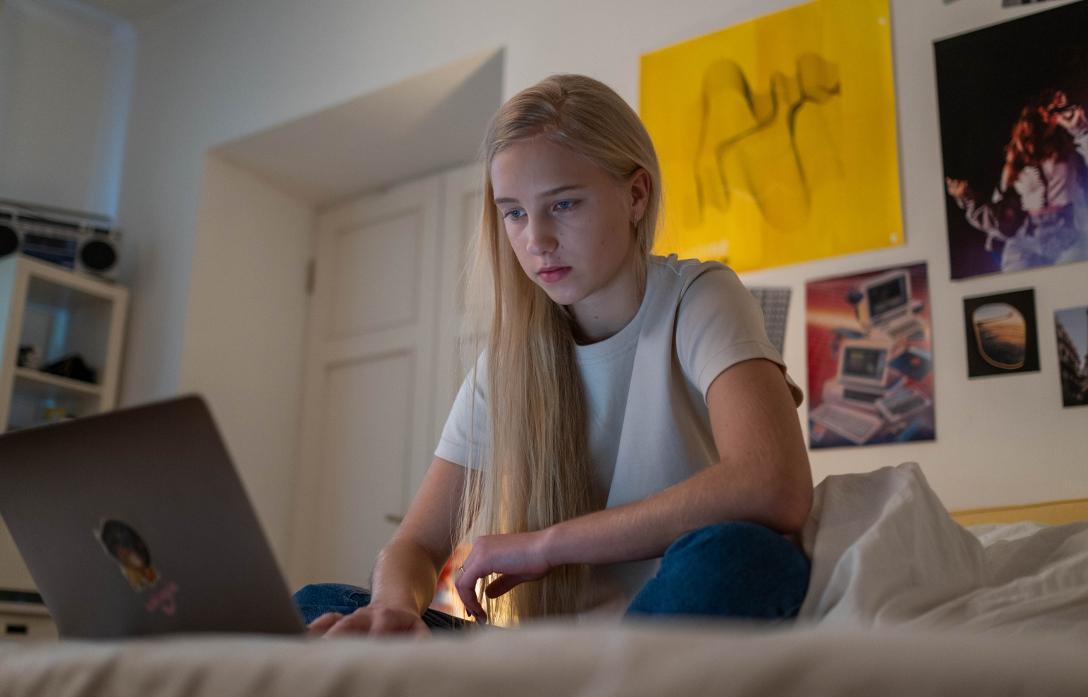 Teenage girl sitting on her bed looking at her laptop.