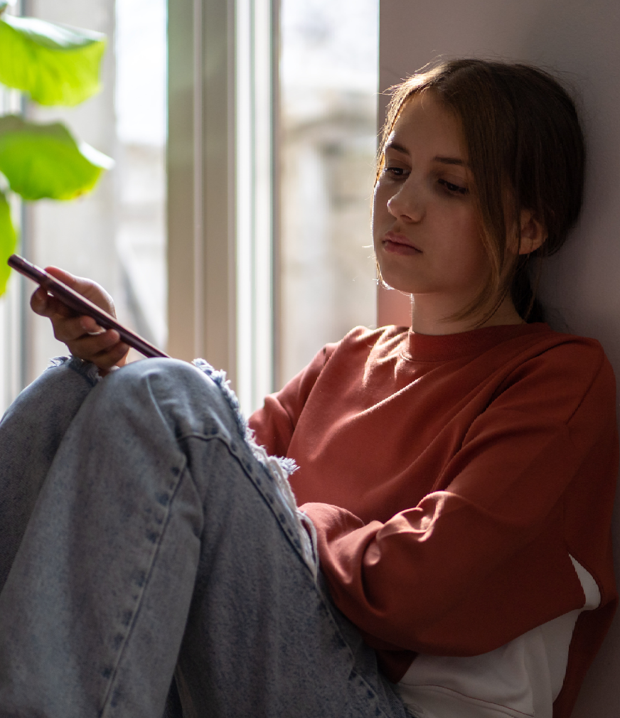 Teenage girl sitting against a wall looking at her phone.