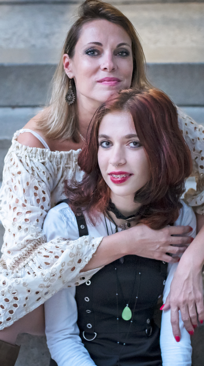 A woman is sitting next to a young girl on a set of stairs.