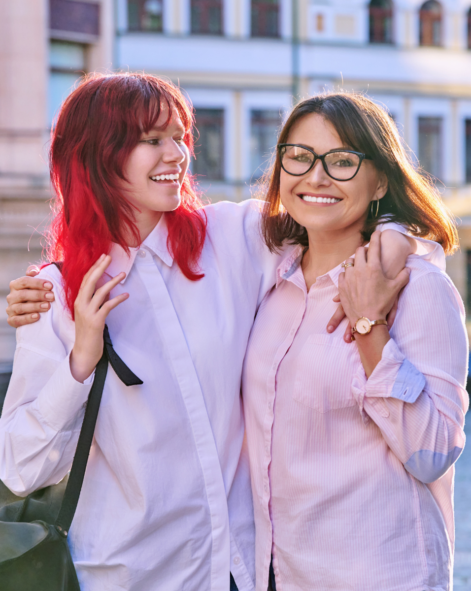 A woman with red hair is hugging another woman with glasses.