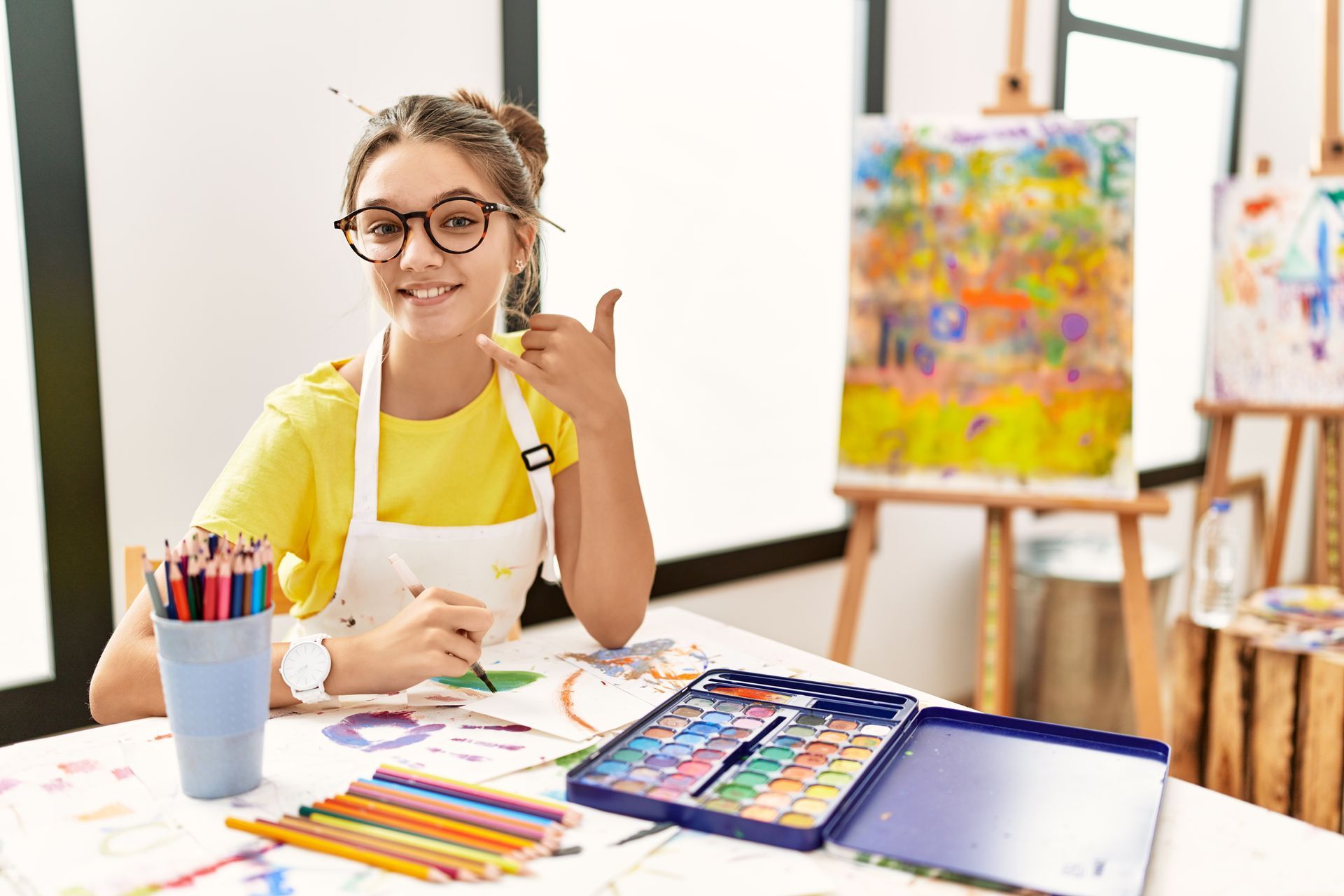 A young girl is sitting at a table in front of an easel.