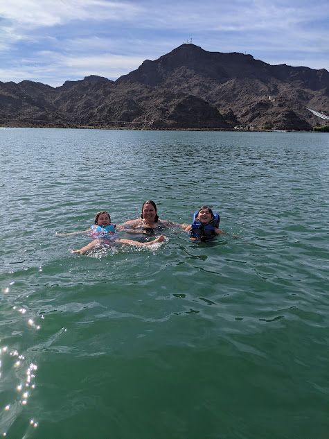 Three people are swimming in a lake with mountains in the background.