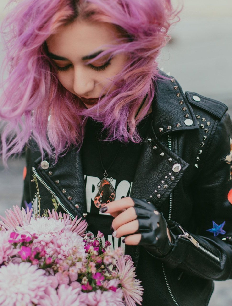 A woman with pink hair is wearing a black leather jacket and holding a bouquet of flowers.