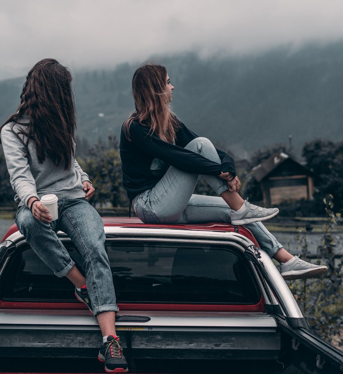 Two women are sitting on the back of a truck.