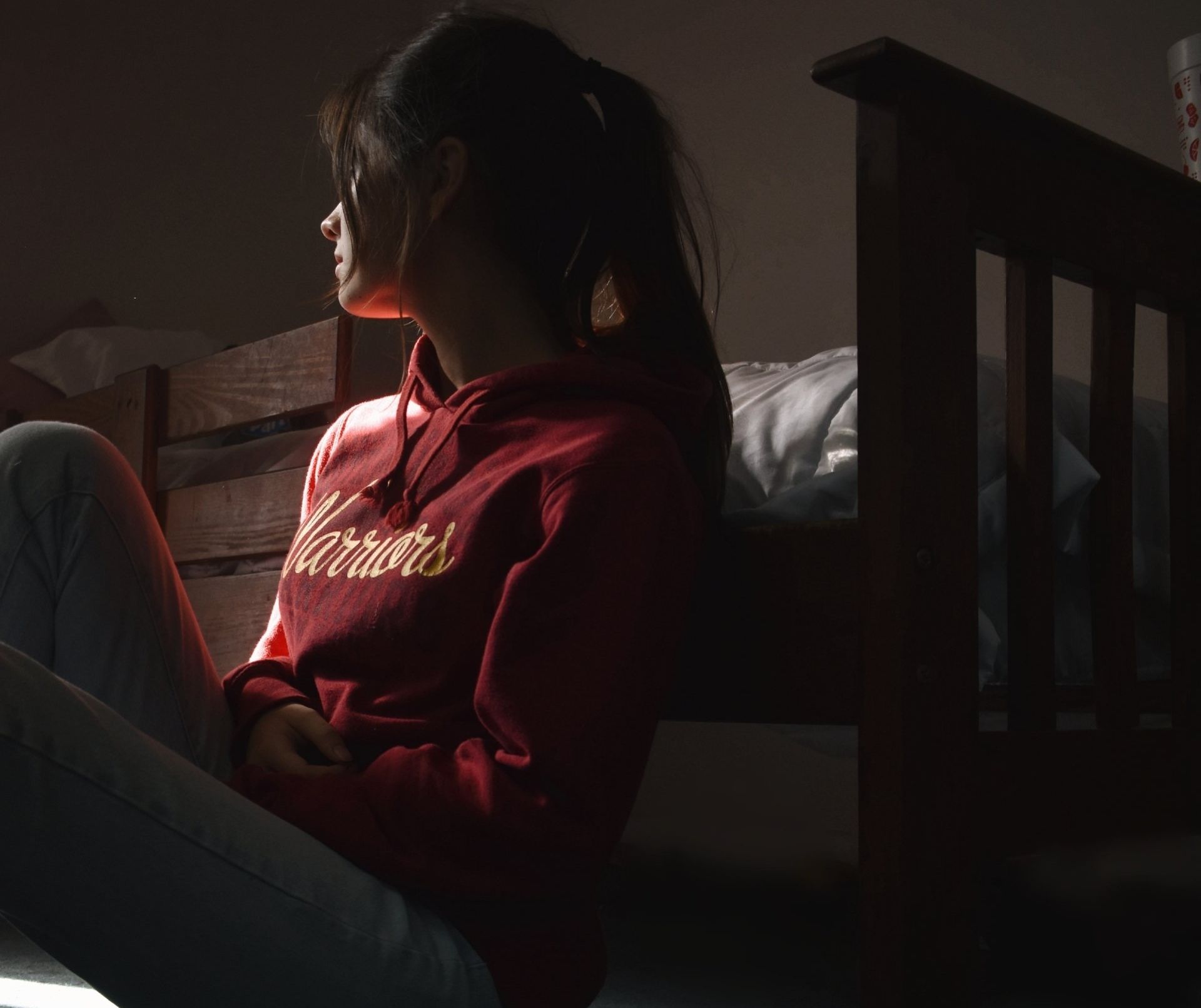 A woman wearing a red varsity sweatshirt sits on a bed