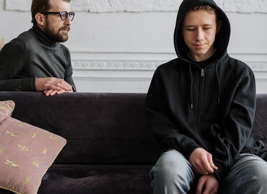 A man and a boy are sitting on a couch talking to each other.