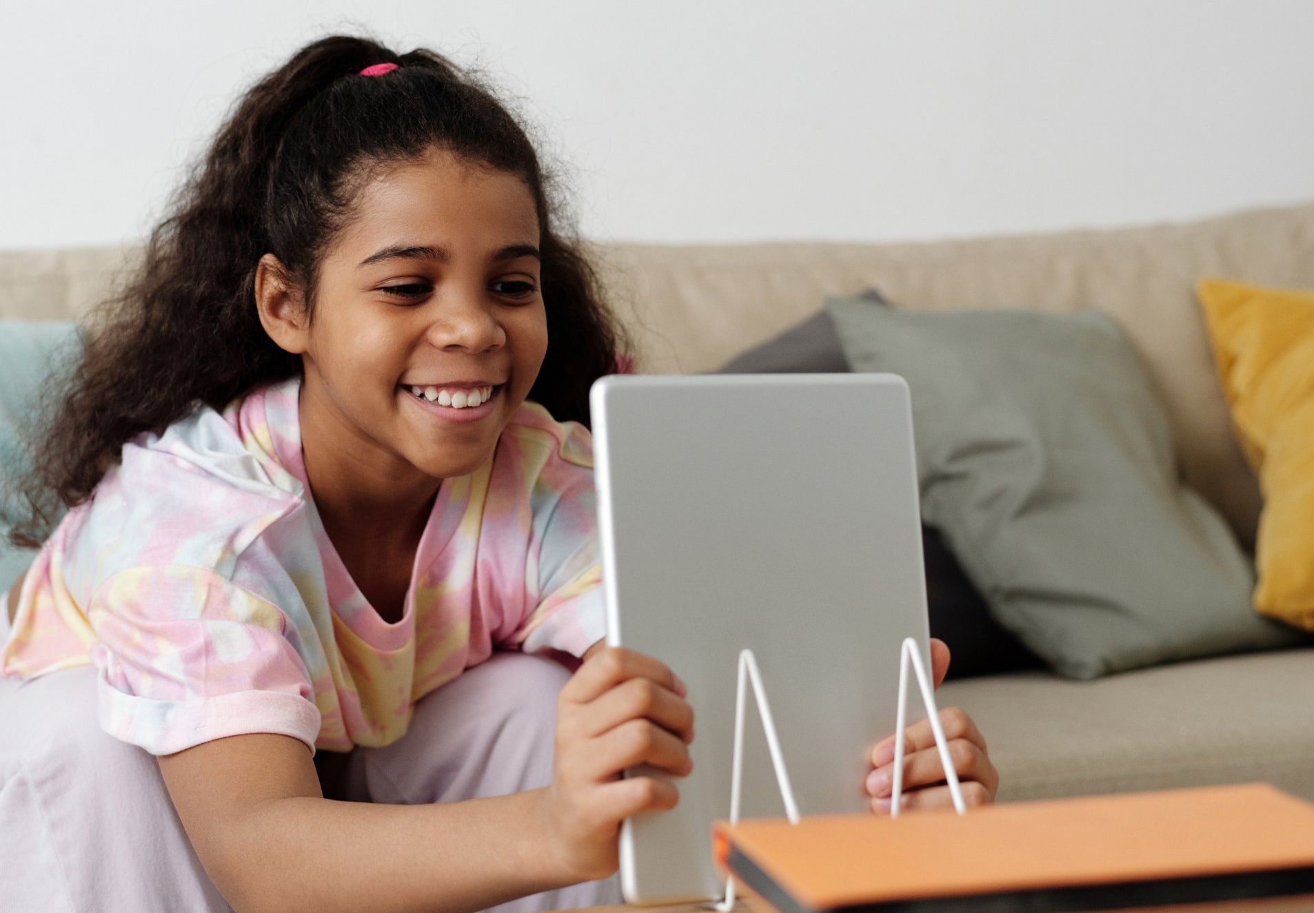 A young girl is sitting on a couch using a tablet computer.