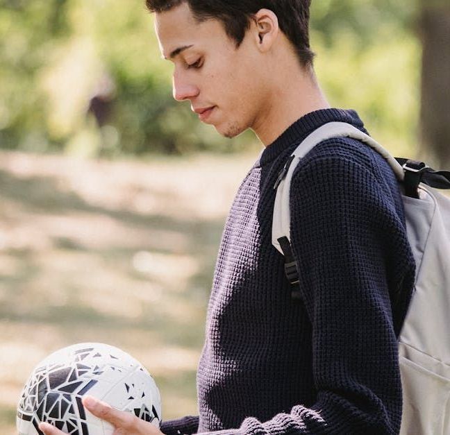 A young man with a backpack is holding a soccer ball