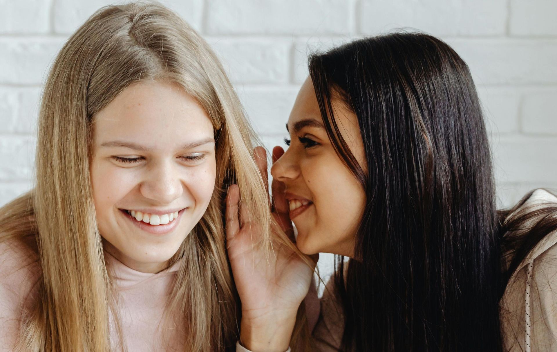 Teenage girl whispering into another teenage girl's ear
