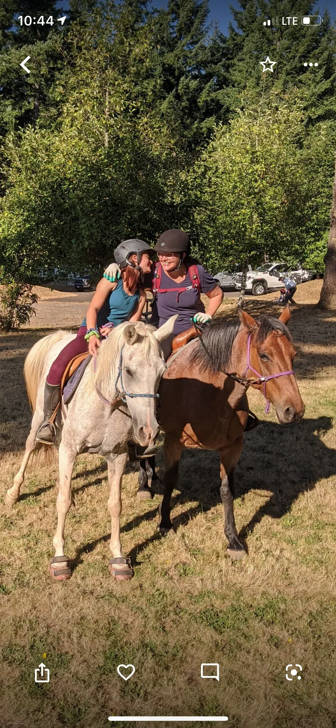 A parent and their teen are riding horses in a field.