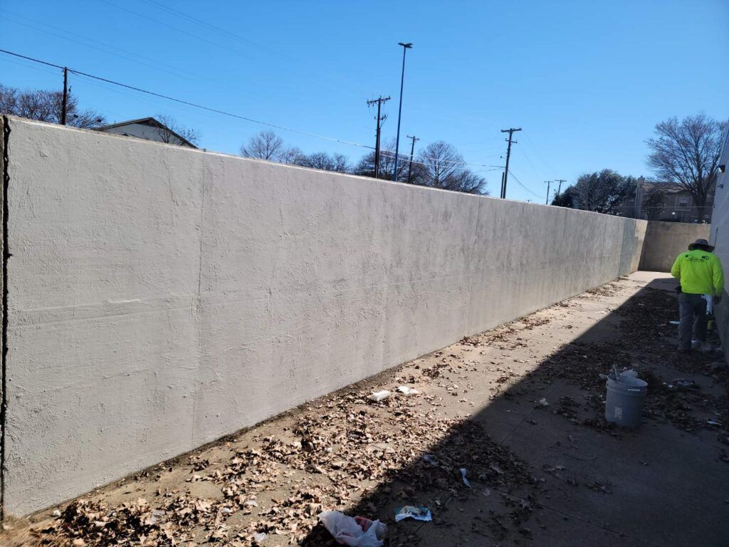 after-graffiti-1 Concrete wall alongside a narrow path with a person in a safety vest.