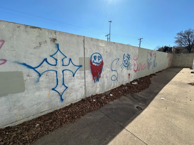 before-graffiti-1 Concrete wall with graffiti art: cross, face, cat, text. Dry leaves and blue sky.