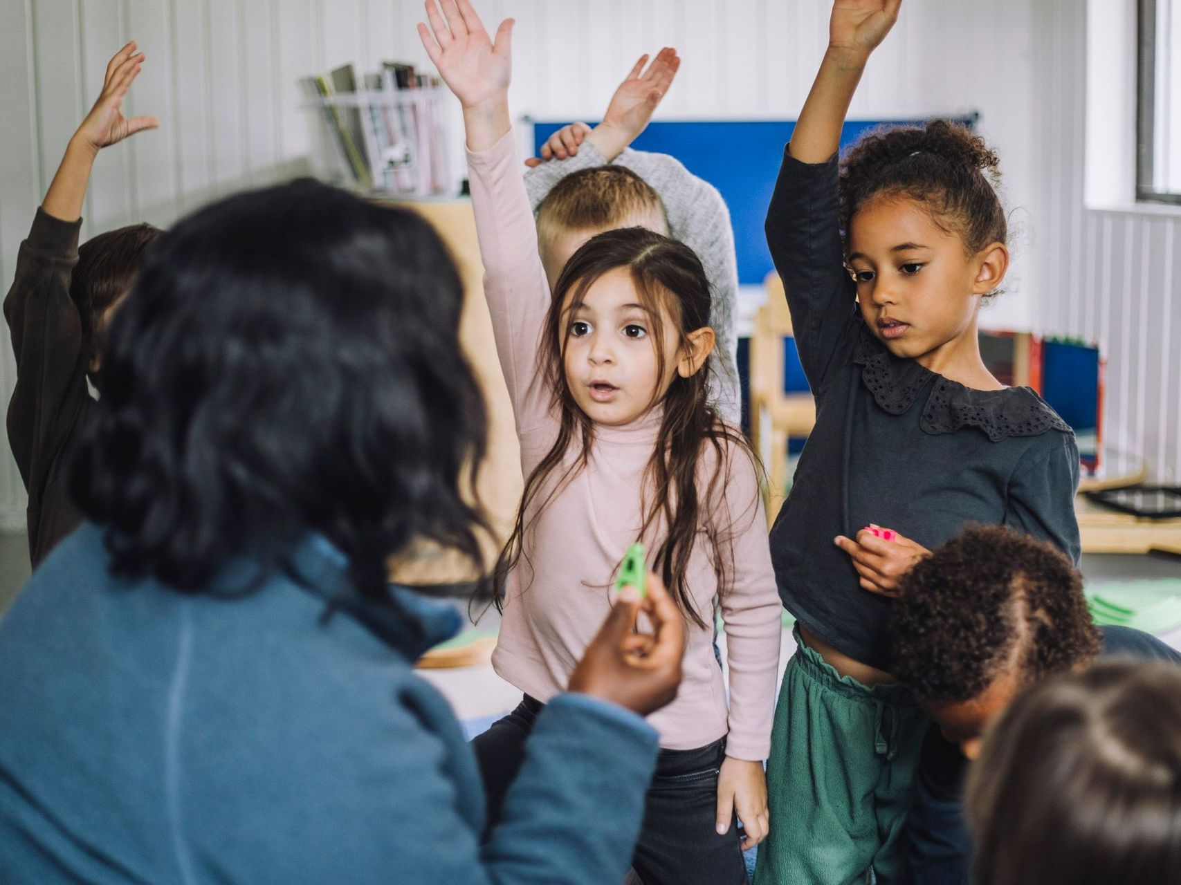 A group of children are raising their hands to answer a question in a classroom. A group of children is raising their hands to answer a question in a classroom.