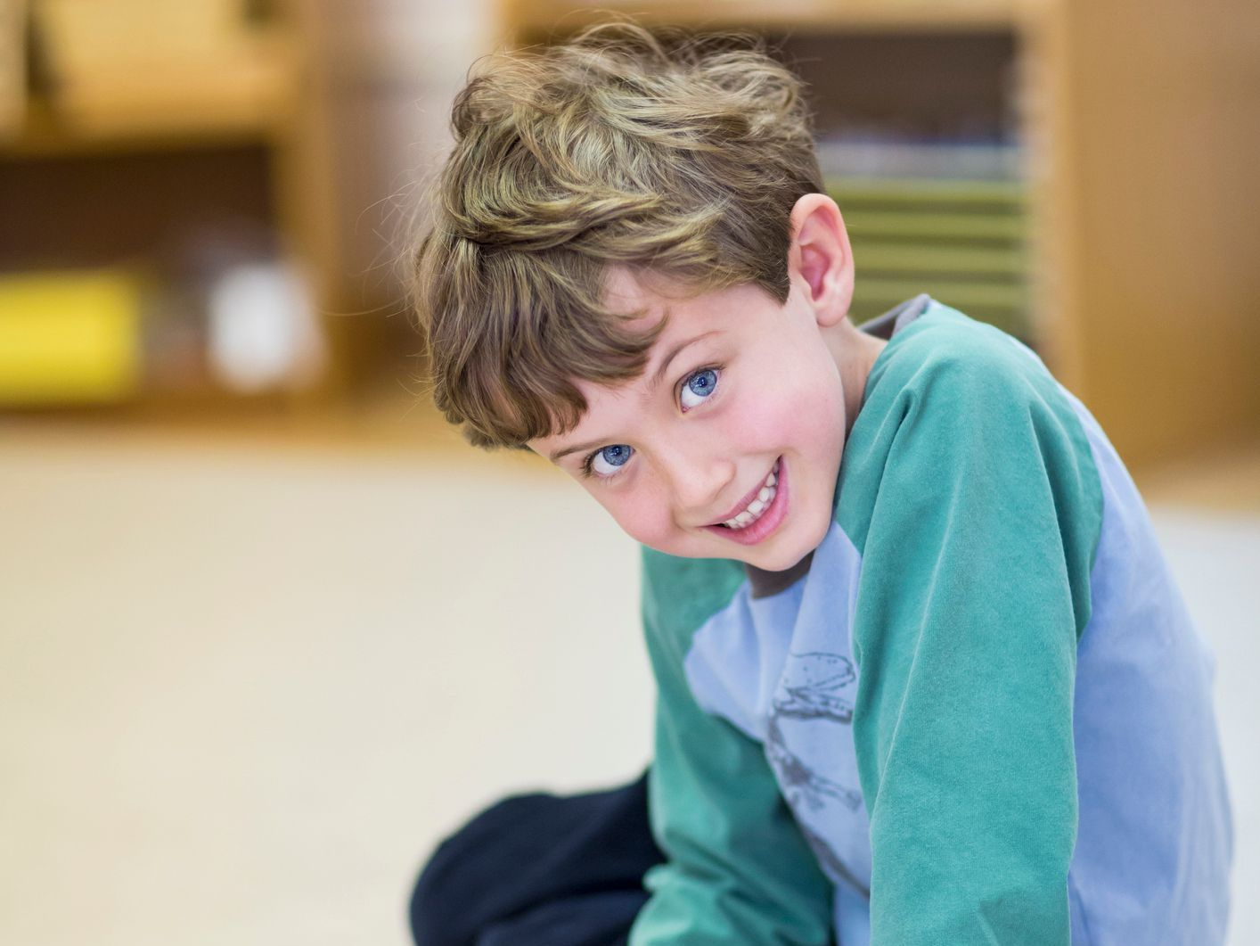 A young boy is sitting on the floor smiling for the camera. A young boy is sitting on the floor smiling for the camera.
