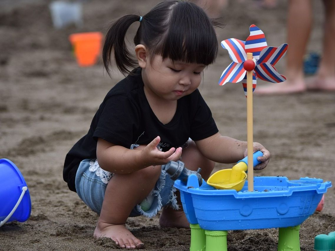 A little girl is playing in the sand with a windmill. A little girl is playing in the sand with a windmill.