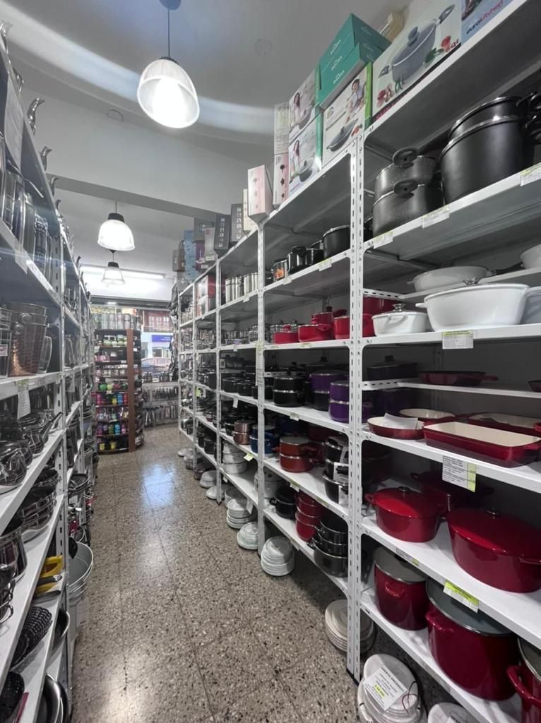 Un pasillo estrecho de tienda con estanterías de metal repletas de ollas, sartenes y utensilios de cocina.