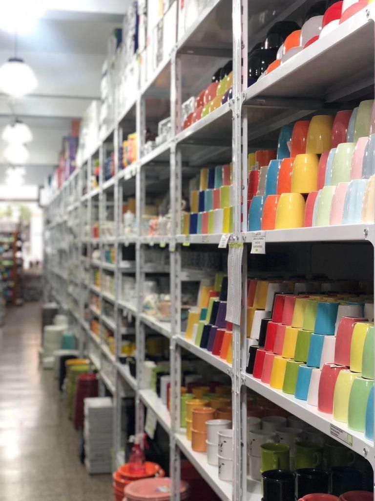Filas de estantes llenos de tazas de colores en una tienda.