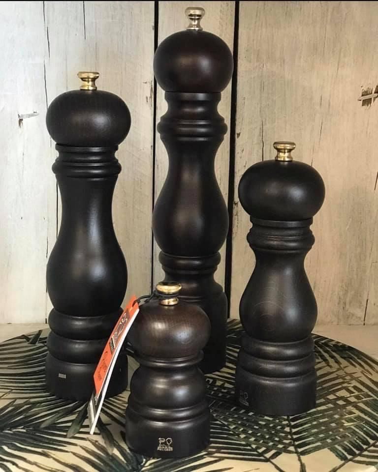Cuatro molinillos de pimienta de madera oscura con tapas doradas sobre una superficie de madera.
