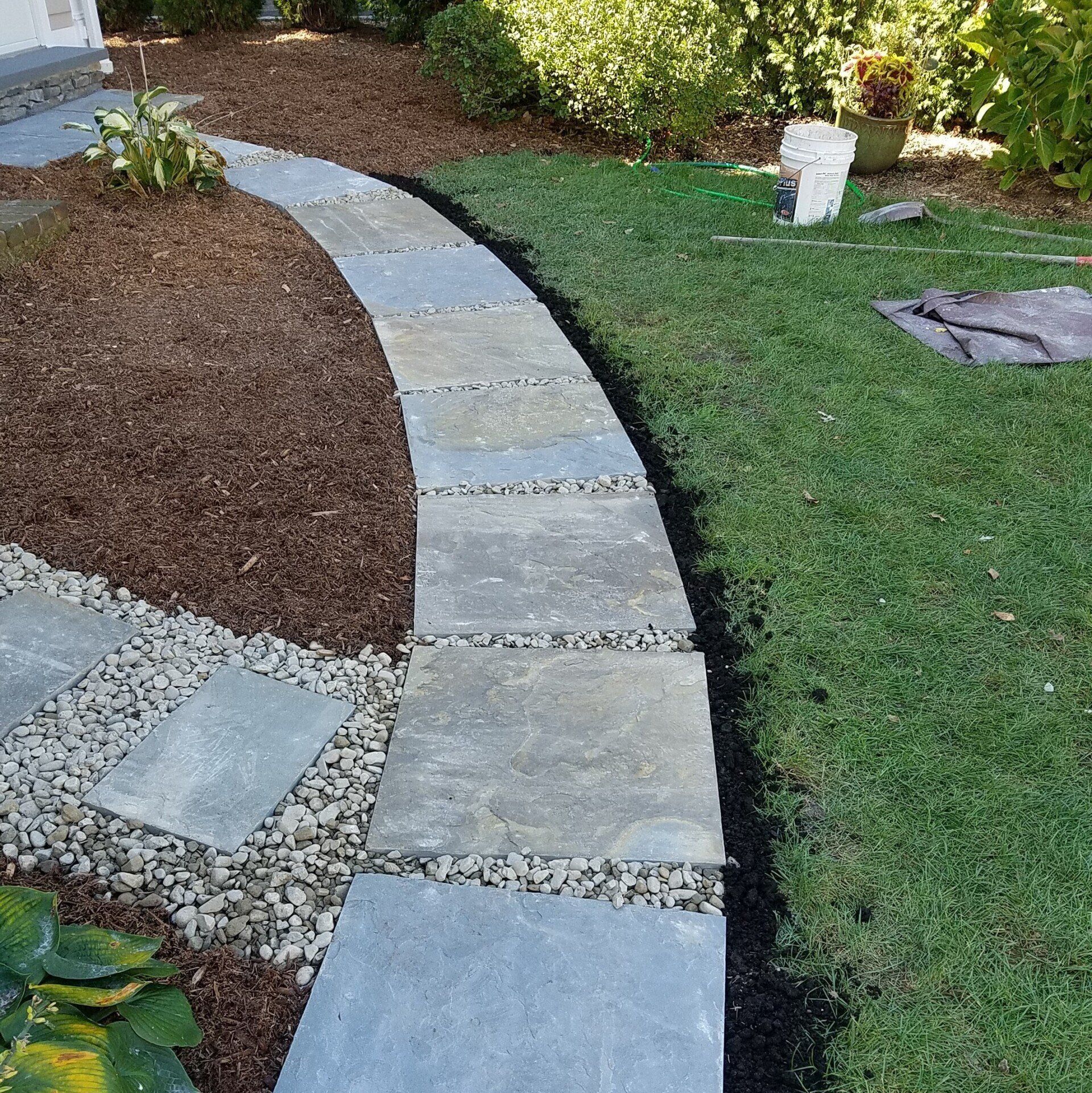 A stone walkway going through a lush green yard, afer photo.