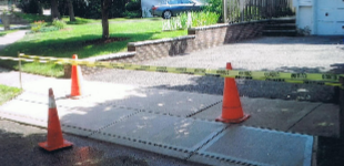 Two orange traffic cones are sitting on a sidewalk in front of a house.