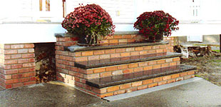 A brick porch with flowers in pots on the steps.
