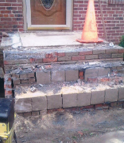 A brick porch with steps under construction n front of a brick house.