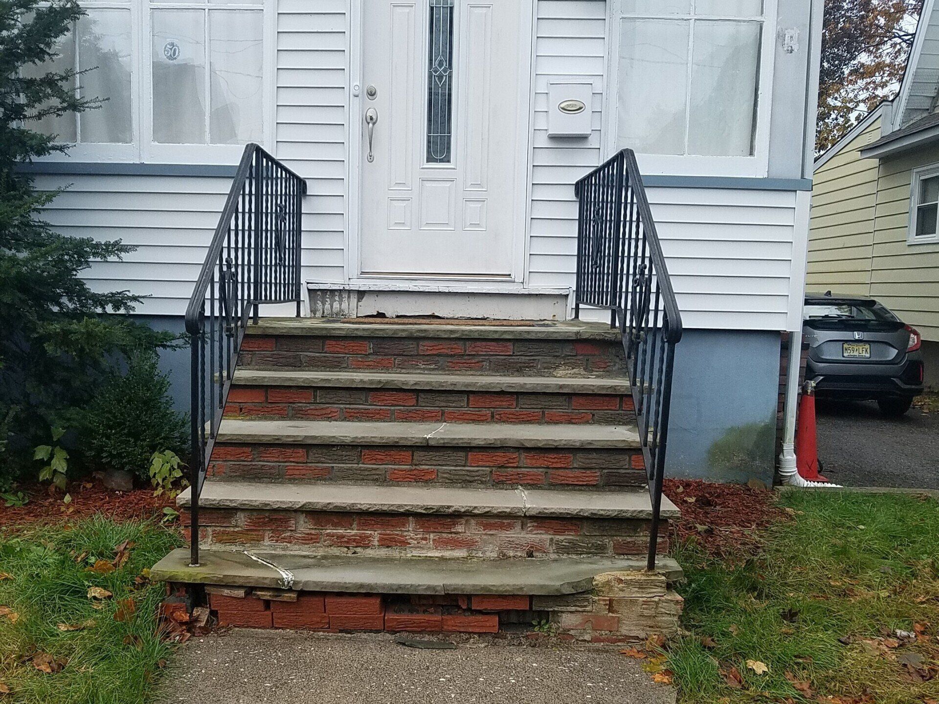 A white house with brick steps and a car parked in front of it.
