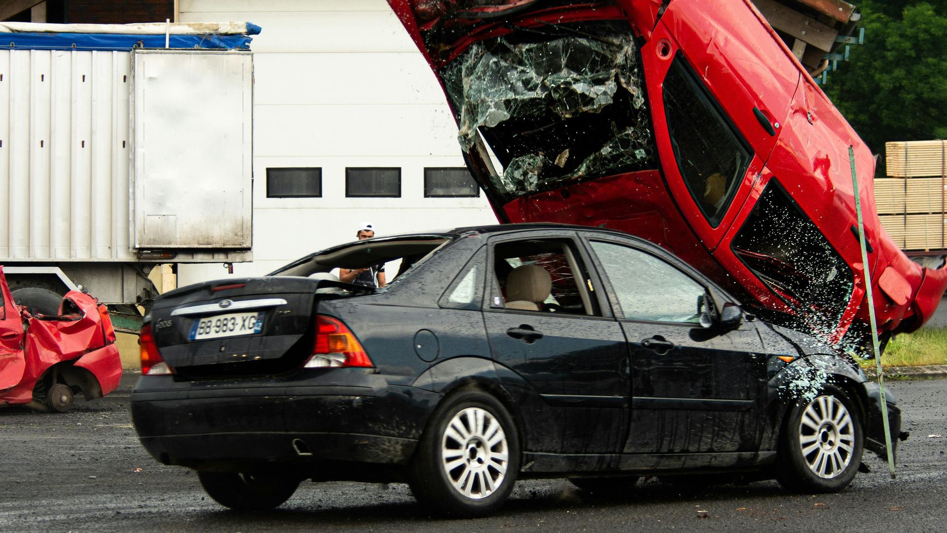 Two damaged cars; red car crushed on top of a black car. Car crash scene, outdoors.