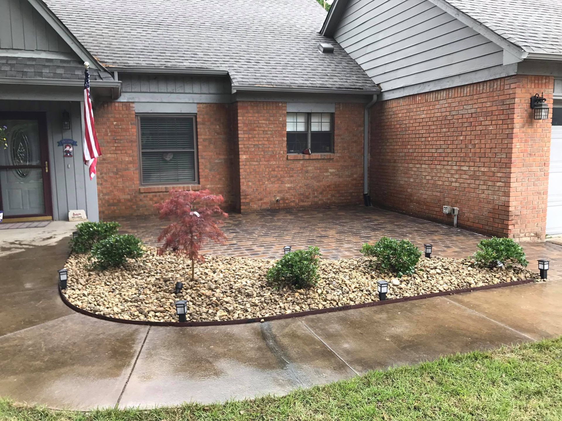 A brick house with a concrete driveway and a garden in front of it.